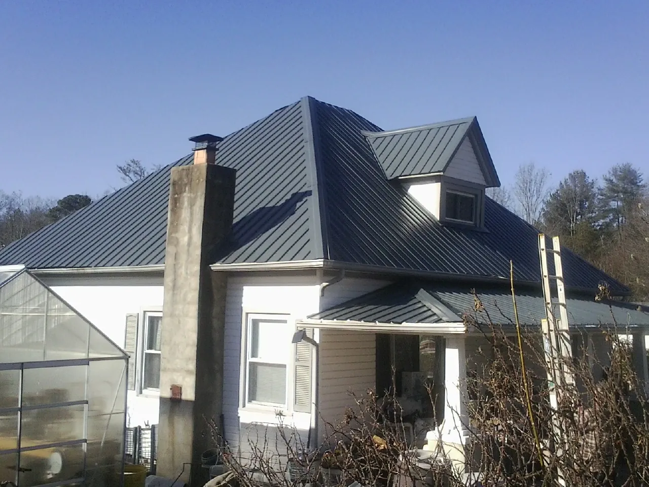 Dark blue standing seam metal roof on a white farmhouse with dormer — Slate & Tile Roof Repair by Roofing Brothers in Onawa