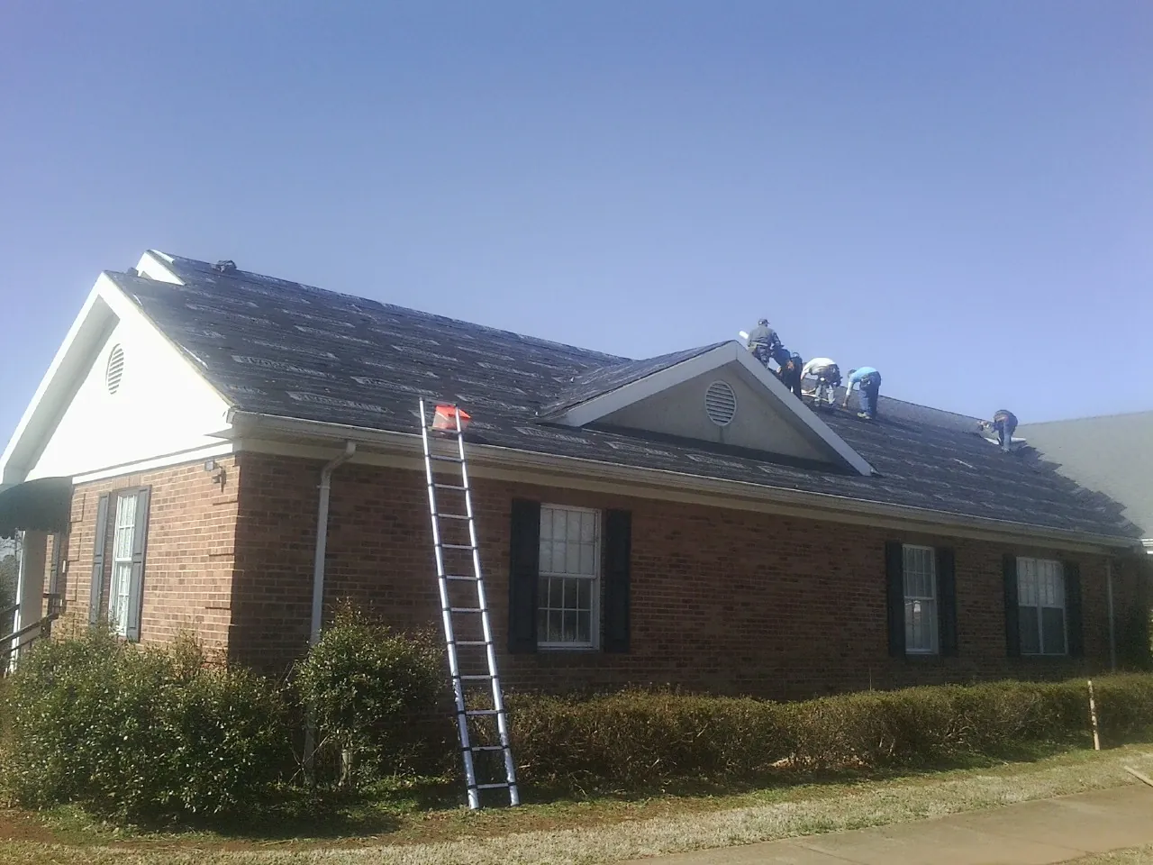 Crew tearing shingles off a brick ranch roof with a ladder set — Metal Roof Repair work by our crew in Onawa