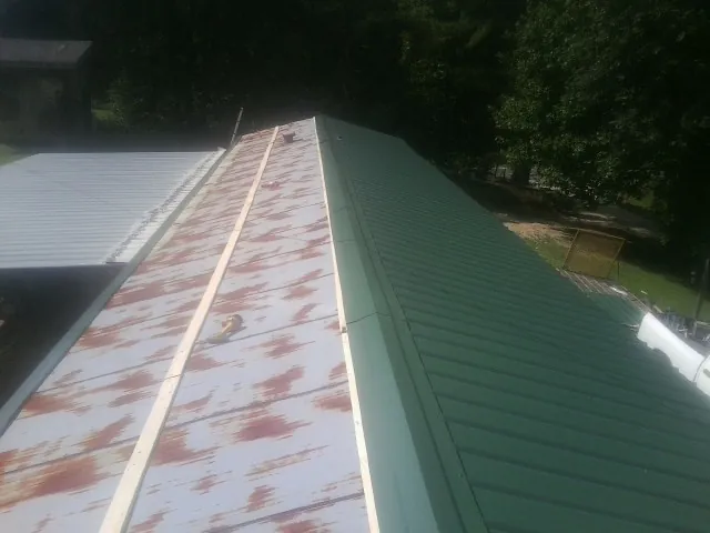 Old rusted panels beside newly installed green metal roofing — Wind Damage Roof Repair by Roofing Brothers in Onawa