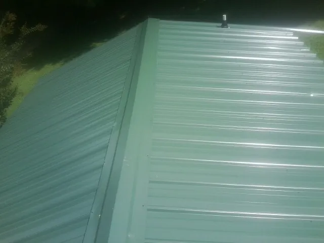 New green metal panels meeting at the ridge of a roof — Flat Roof Repair work by our crew in Onawa
