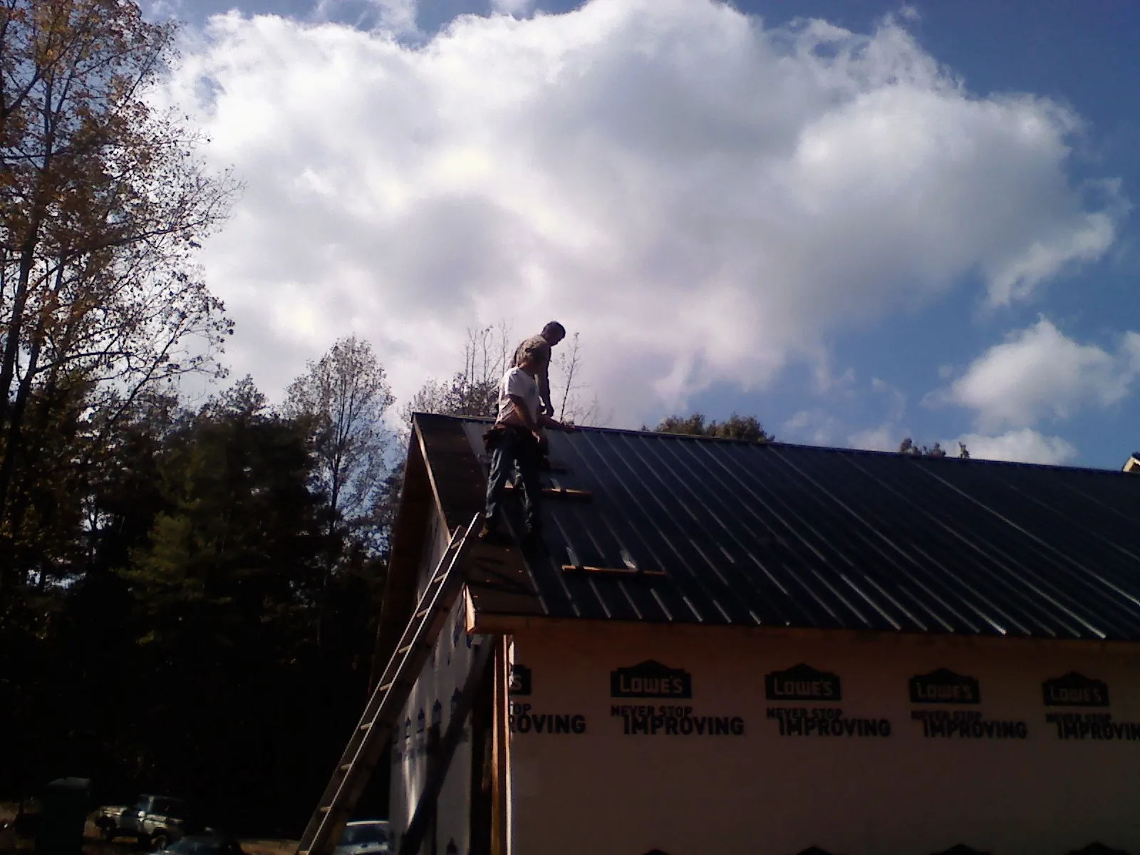 Roofer fastening dark metal panels high against a cloudy sky, from a Roof Inspection job in Onawa