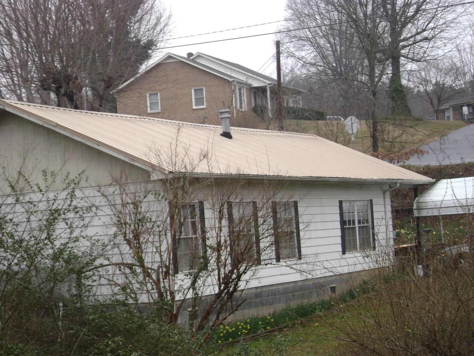 Tan metal roof on a white sided house set into a hillside — Commercial Roofing by Roofing Brothers in Onawa