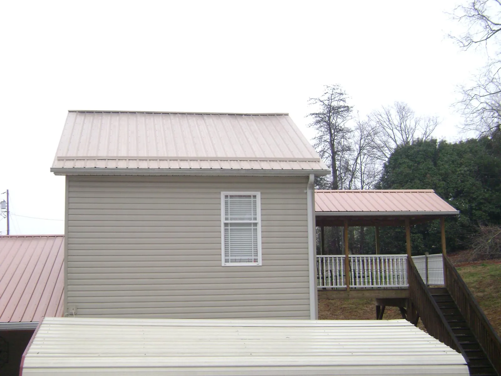 Tan metal roofs on a two story addition and attached porch, from a Roof Replacement job in Onawa